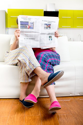 Married couple reading newspaper dressed in pajamas sitting in sofa at home